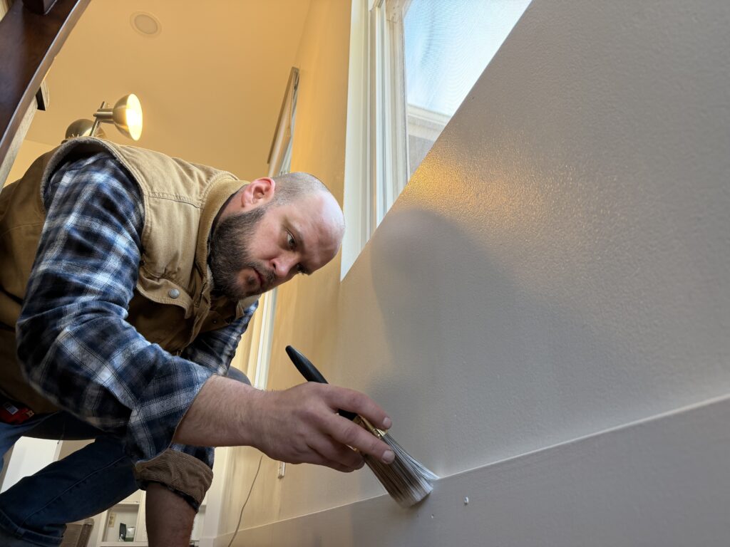 Handyman Dominik painting baseboards white.